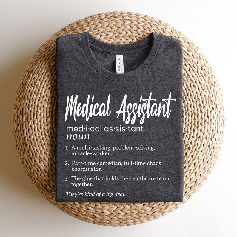 May include: A dark gray t-shirt with white text that reads "Medical Assistant" and a definition of the term. The definition includes the phrase "They're kind of a big deal."
