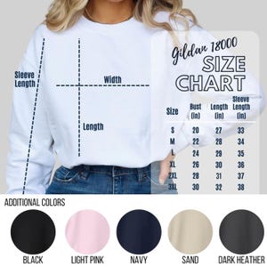 Op de afbeelding: Een wit Gildan 18000 sweatshirt met een maattabel die de buste, lengte en mouwlengte in inches weergeeft voor de maten S tot 3XL. Hieronder staan vijf cirkelvormige kleurstaaltjes, gelabeld als black, light pink, navy, sand, dark heather.