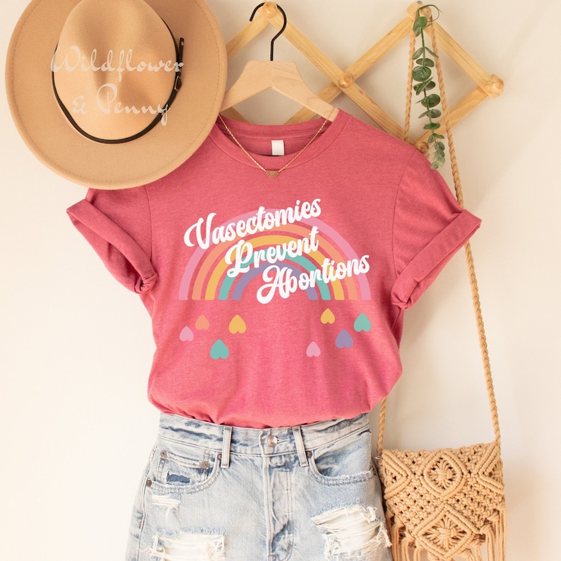 Pu&ograve; includere: Una maglietta rosa con una grafica arcobaleno e il testo "Vasectomies Prevent Abortions". La maglietta ha un arcobaleno con cuori sotto.