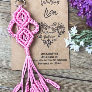 May include: Pink macrame keychain with a tassel and a card that says "Alles liebe zum Geburtstag Lisa" and "Das Geheimnis des Glücks ist, statt der Kerzen die schönen Momente zu zählen."