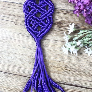 May include: Purple macrame keychain with a tassel and a metal ring. The keychain is made of knotted cord and has a decorative design.