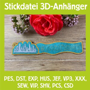 Puede incluir: Una pancarta bordada en color turquesa y dorado con la palabra "STADTKIND" y un diseño de paisaje urbano. La pancarta está colocada sobre un fondo de madera, con una rosa roja y ramitas de flores en el fondo. El texto "Stickdatei 3D-Anhänger" está en la parte superior.