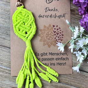 Peut inclure: Un porte-clés en macramé vert vif avec un pompon. Le porte-clés est attaché à une carte avec le texte "Lisa Danke das es dich gibt Es gibt Menschen, die passen einfach genau ins Herz!"
