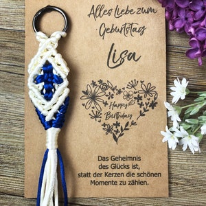 May include: A white and blue macrame keychain with a key ring. The keychain is on a brown card with the text "Alles liebe zum Geburtstag Lisa" and a heart with the text "Happy Birthday".
