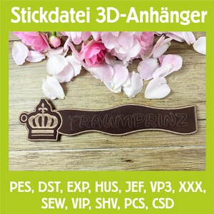 Könnte beinhalten: Ein braunes, gesticktes Banner mit dem Wort "TRAUMPRINZ" und einem Kronen-Design. Das Banner befindet sich vor einem Holzgrund mit rosa Blütenblättern und dem Text "Stickdatei 3D-Anhänger".