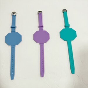 May include: Three silicone wristbands with a stop sign shape. The wristbands are blue, purple, and teal.