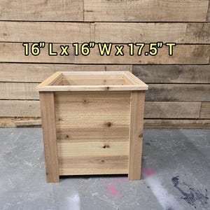 May include: A wooden planter box with a natural finish. The planter is 16 inches long, 16 inches wide, and 17.5 inches tall.  16" L x 16" W x 17.5" T