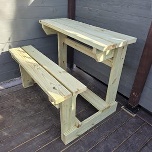 May include: A wooden table and bench set with a natural wood finish. The table has a simple design with a flat top and a single support beam. The bench is attached to the table and has a simple design with two support beams.