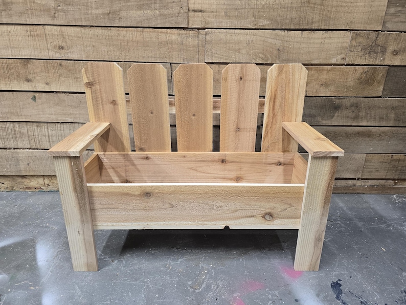 May include: A wooden bench with a planter box built in. The bench has a picket fence style back and is made of natural wood.