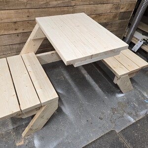 May include: A wooden picnic table with two benches. The table is made of unfinished wood and has a simple design. The benches are attached to the table and fold up for easy storage.