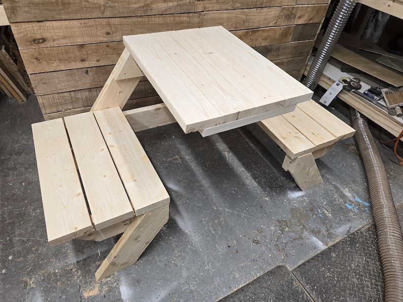 May include: A wooden picnic table with two benches. The table is made of unfinished wood and has a simple design. The benches are attached to the table and fold up for easy storage.