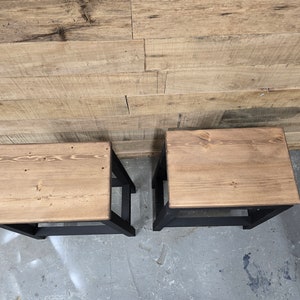 Puede incluir: Dos taburetes de madera con patas pintadas de negro y una tapa de madera natural.