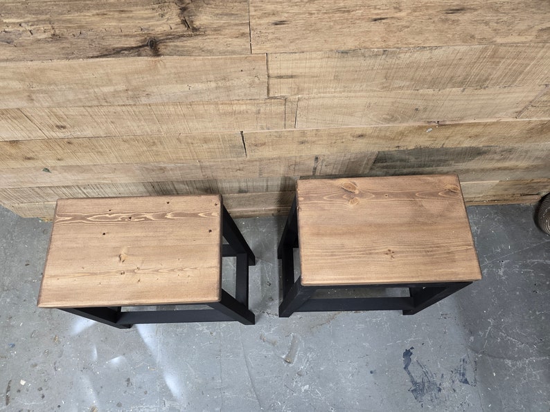 Puede incluir: Dos taburetes de madera con patas pintadas de negro y una tapa de madera natural.