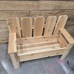 May include: A wooden bench with a planter box built in. The bench is made of natural wood and has a picket fence design on the back.