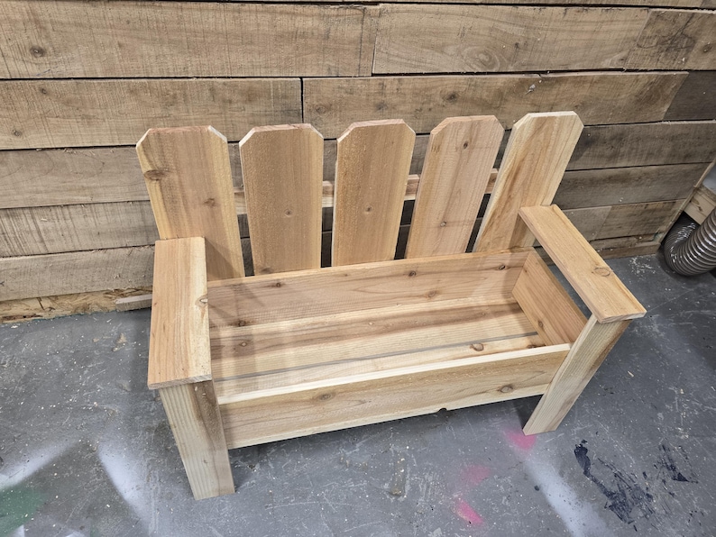 May include: A wooden bench with a planter box built in. The bench is made of natural wood and has a picket fence design on the back.