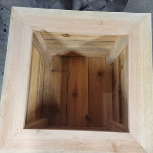 K&ouml;nnte beinhalten: Ein quadratischer Pflanzenkasten aus Holz mit einer nat&uuml;rlichen Holzoptik. Der Pflanzenkasten ist leer und bereit, mit Pflanzen bef&uuml;llt zu werden.