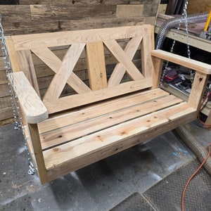 May include: A wooden swing bench with a slatted seat and a decorative X-shaped back. The swing is hanging from chains.