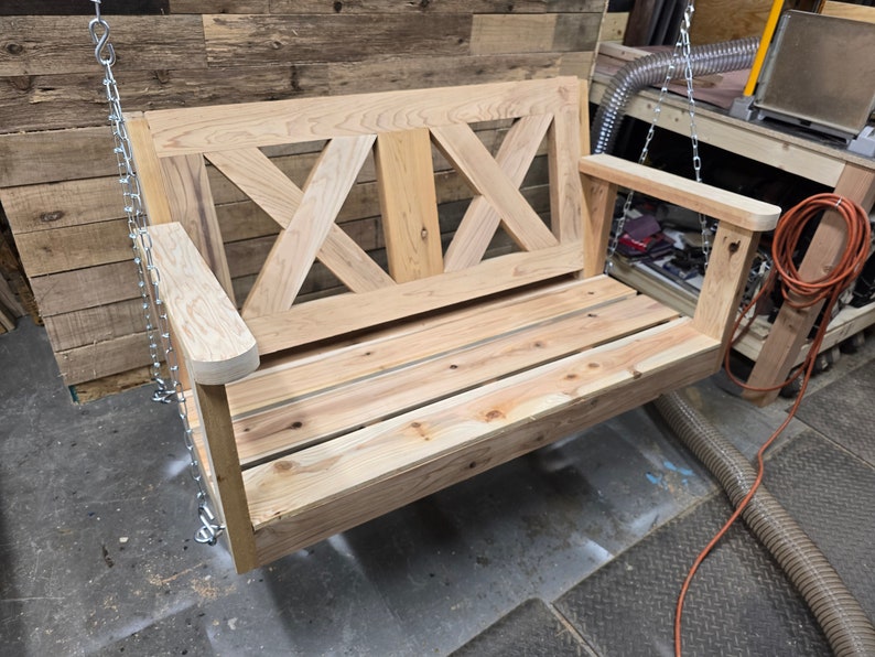 May include: A wooden swing bench with a slatted seat and a decorative X-shaped back. The swing is hanging from chains.