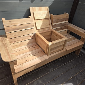 May include: A wooden bench with a built-in storage box. The bench is made of natural wood and has a rustic look. The storage box is located in the center of the bench and has a hinged lid.