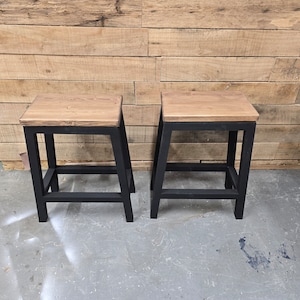 Puede incluir: Dos taburetes de madera con marcos de metal negro. Los taburetes tienen un acabado de madera natural y son de un dise&ntilde;o simple y moderno.