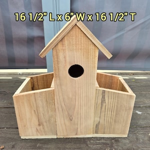 May include: A wooden birdhouse with a peaked roof and a circular entry hole. The birdhouse has two open compartments on either side. The dimensions are 41.9 cm L x 15.2 cm W x 41.9 cm T.