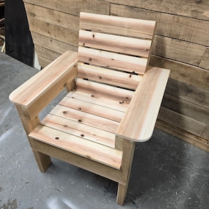 May include: A wooden chair with a slatted back and armrests. The chair is made of unfinished wood and has a natural color.