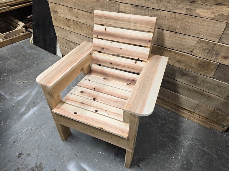 May include: A wooden chair with a slatted back and armrests. The chair is made of unfinished wood and has a natural color.
