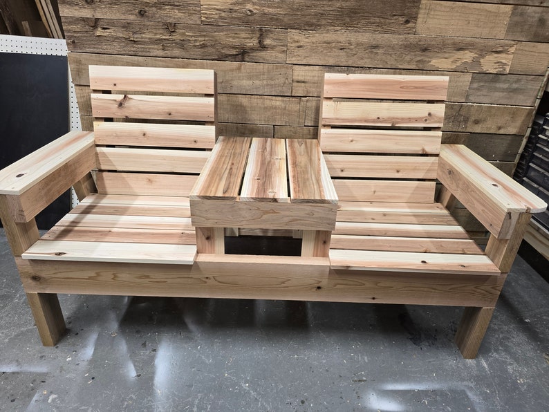 Pu&ograve; includere: Una panca in legno con un tavolo integrato al centro. La panca &egrave; realizzata in legno naturale e ha un aspetto rustico. Ha due posti a sedere e un piccolo tavolo al centro.