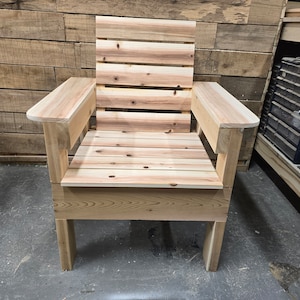 May include: A wooden chair with a slatted back and armrests. The chair is made of unfinished wood and has a simple design.