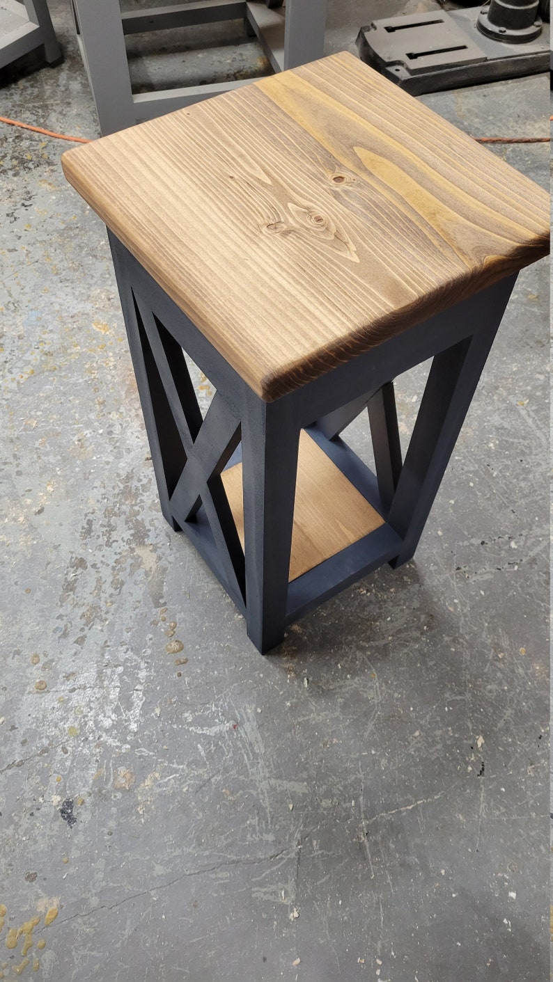 May include: A small wooden side table with a dark blue painted frame and a natural wood top. The table has a geometric design with a shelf underneath the top.