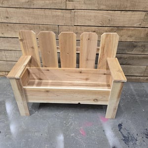 May include: A wooden bench with a planter box built in. The bench is made of natural wood and has a simple design. The planter box is empty and ready for plants.