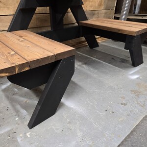 May include: A black wooden picnic table with two benches. The table and benches are made of wood with a dark brown stain. The table is in a workshop setting.
