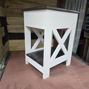 May include: White end table with a black stained top and shelf. The table has an X-shaped design on the front.