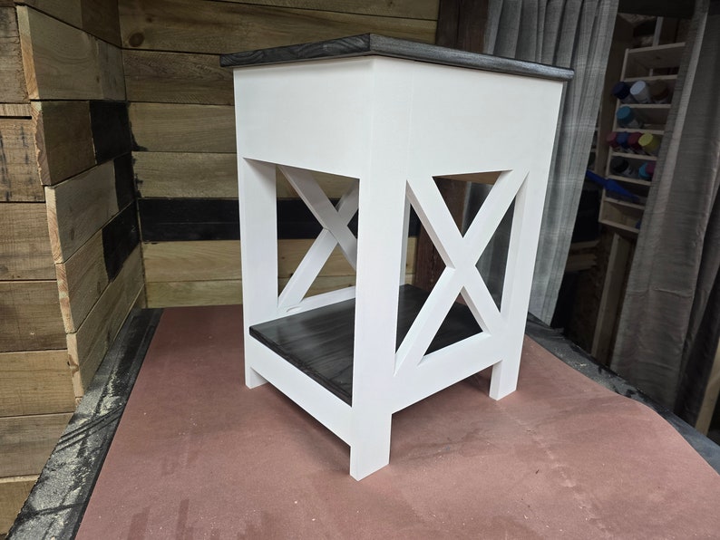 May include: White end table with a black stained top and shelf. The table has an X-shaped design on the front.