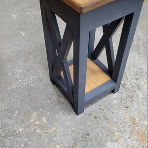 May include: A dark blue wooden end table with a light brown wood top and a shelf. The table has an X-shaped design on the sides.