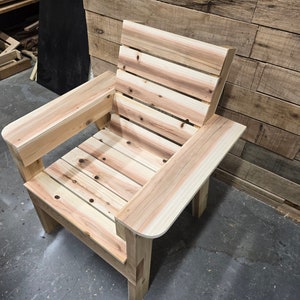 May include: A wooden chair with a slatted back and seat. The chair has a single armrest on the left side and is made of light-colored wood.
