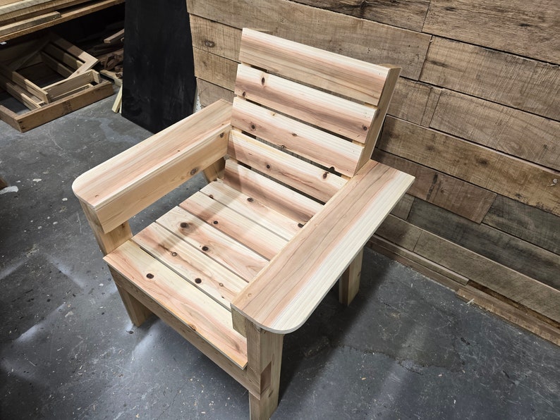 May include: A wooden chair with a slatted back and seat. The chair has a single armrest on the left side and is made of light-colored wood.
