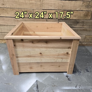 May include: A wooden planter box with a natural wood finish. The planter is 24 inches wide, 24 inches long, and 17.5 inches tall.
