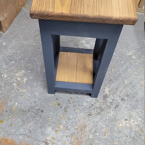 May include: A small wooden side table with a dark blue painted frame and a natural wood top and shelf. The table has a simple design with a single shelf.