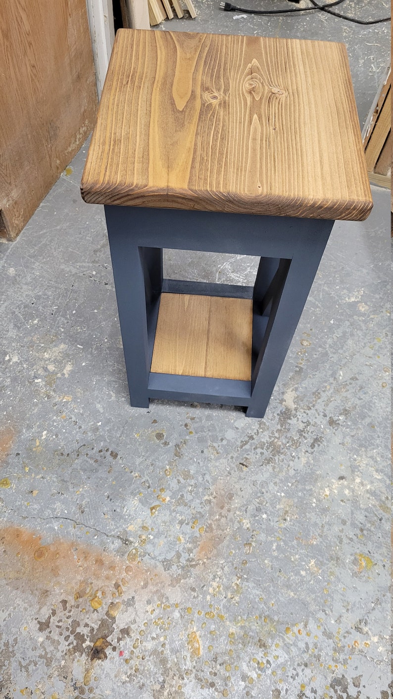 May include: A small wooden side table with a dark blue painted frame and a natural wood top and shelf. The table has a simple design with a single shelf.