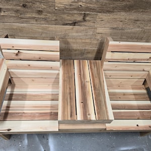 Pu&ograve; includere: Una panca in legno con due posti a sedere e un tavolino al centro. La panca &egrave; realizzata in legno naturale di colore marrone chiaro.