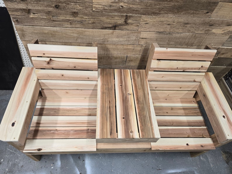 Pu&ograve; includere: Una panca in legno con due posti a sedere e un tavolino al centro. La panca &egrave; realizzata in legno naturale di colore marrone chiaro.