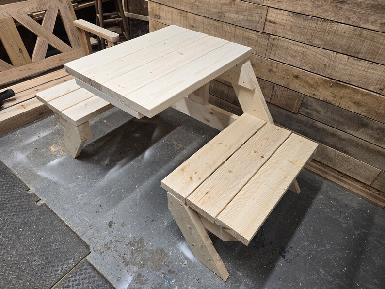 May include: A wooden picnic table with two benches. The table is made of unfinished pine wood and has a simple design. The benches are attached to the table and fold up for easy storage.