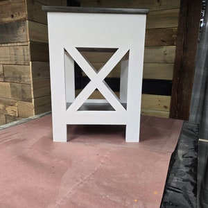 May include: White wooden end table with a gray top and an X-shaped design on the front. The table has a shelf and four legs.