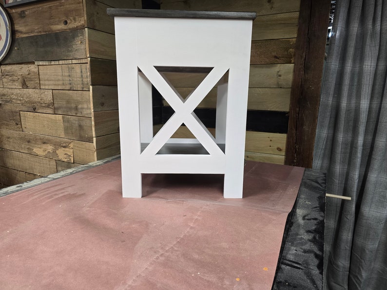 May include: White wooden end table with a gray top and an X-shaped design on the front. The table has a shelf and four legs.