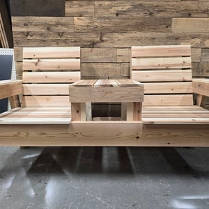 Pu&ograve; includere: Una panca in legno con due posti a sedere e un tavolino al centro. La panca &egrave; realizzata in legno naturale e ha un aspetto rustico.