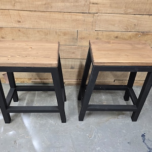 Puede incluir: Dos taburetes de metal negro con tapas de madera. Los taburetes tienen un dise&ntilde;o sencillo con un solo estante.