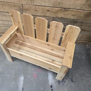 May include: A wooden planter bench with a picket fence design. The bench has a rectangular planter box and a back with vertical slats.