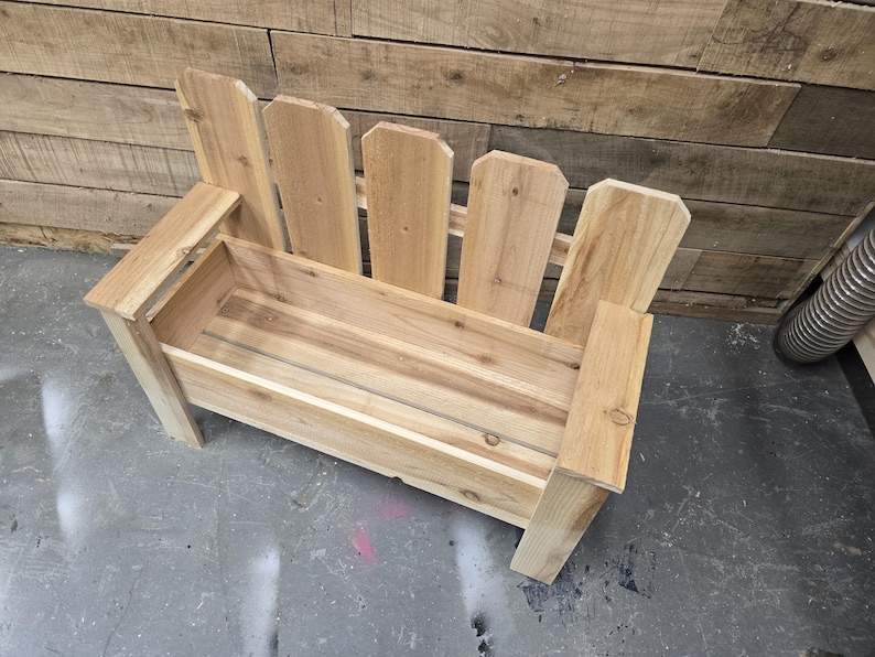 May include: A wooden planter bench with a picket fence design. The bench has a rectangular planter box and a back with vertical slats.