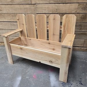 May include: A wooden bench with a planter box built in. The bench has a picket fence style back and is made of natural wood.